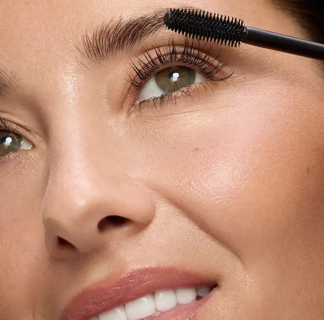 Close-up of a woman using a spoolie brush to groom her eyebrows.