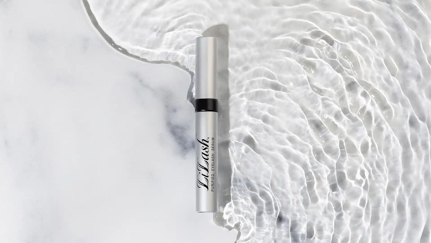 LiLash Purified Eyelash Serum tube on white marble surface with water ripples for beauty enhancement