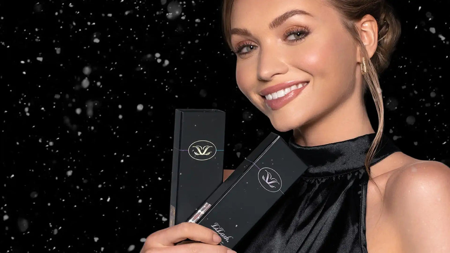Smiling woman with long lashes and defined brows holding black LiLash beauty serum boxes against a starry black background
