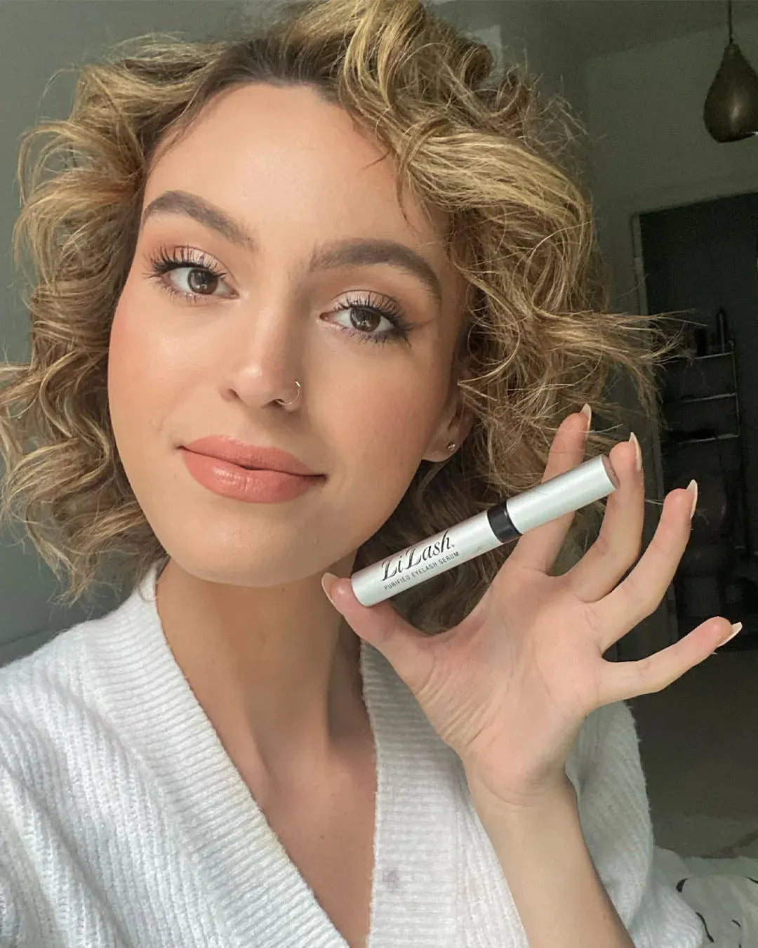 Woman holding LiLash purified eyelash serum, showcasing longer, fuller lashes with natural makeup look