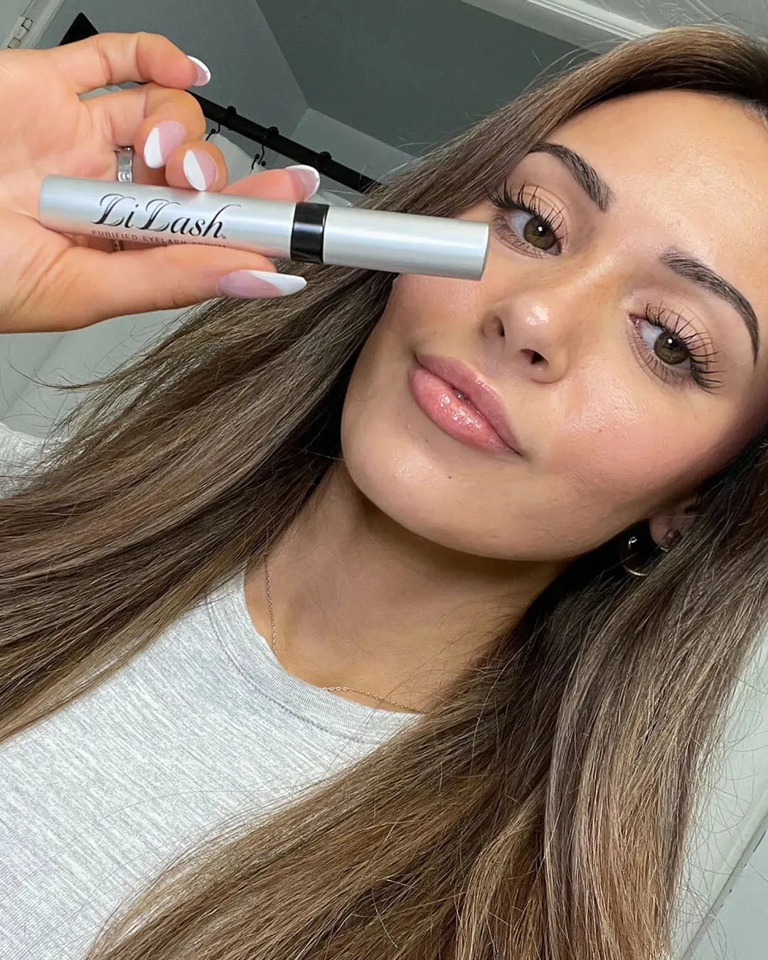 Woman holding LiLash eyelash serum, showcasing long, full lashes for natural beauty enhancement