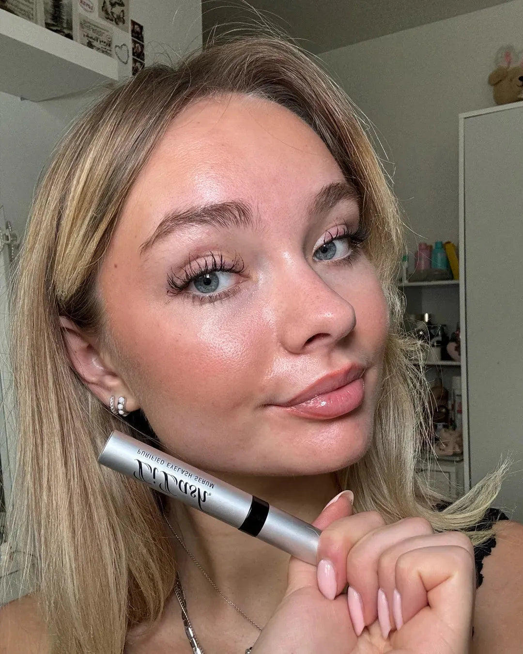 Woman holding eyelash serum pen, showcasing long, full lashes with natural makeup look
