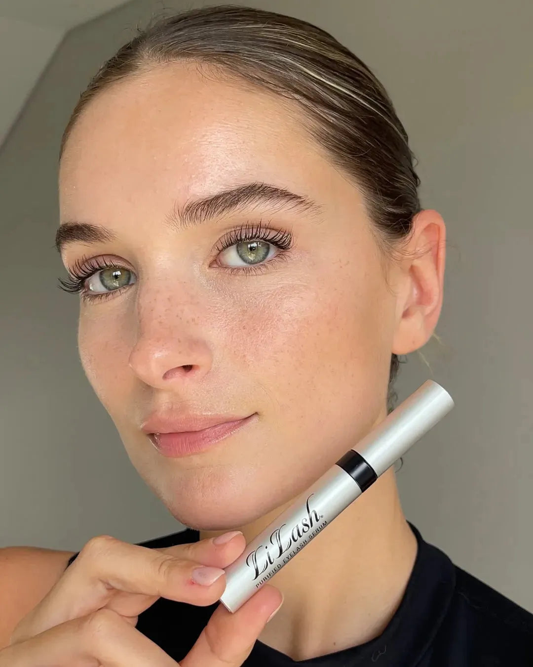 Woman holding LiLash purified eyelash serum for longer, fuller lashes and defined brows