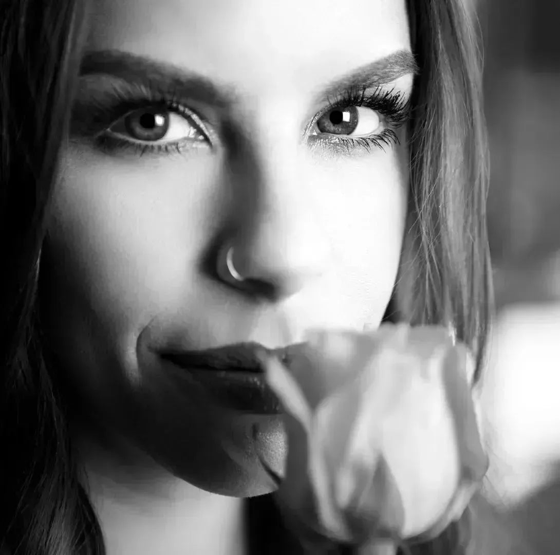Woman with long, full lashes holding a rose, showcasing natural beauty and defined brows.