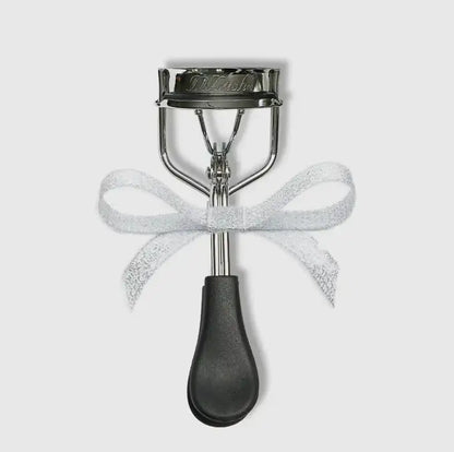 Silver eyelash curler with a white glittery ribbon bow tied around the center.