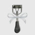 Silver eyelash curler with a white glittery ribbon bow tied around the center.